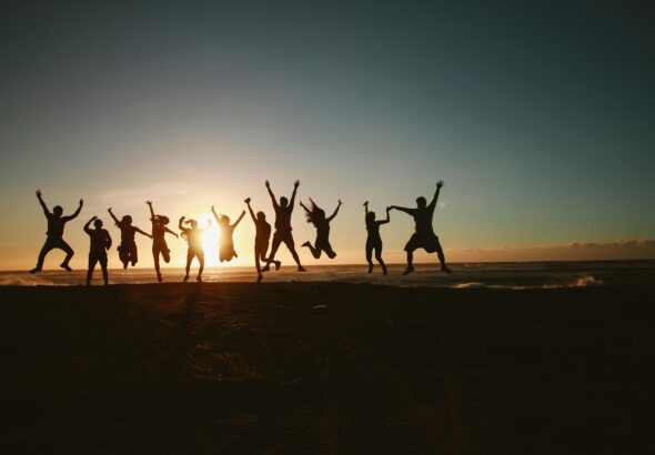 Silhouette of a group of friends jumping on a beach at sunset, expressing joy and freedom.