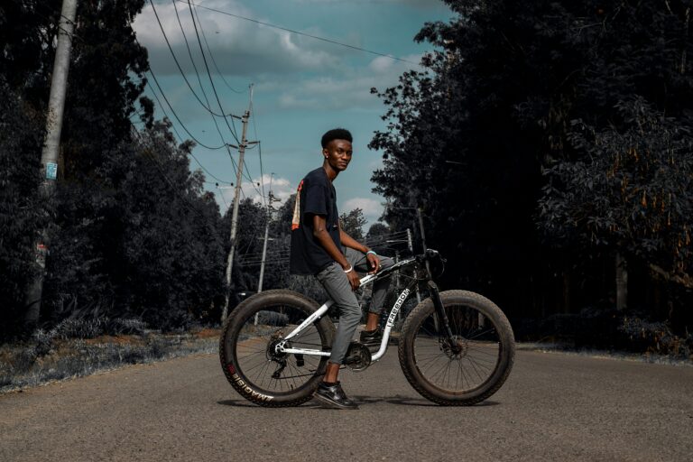 A young man enjoys a peaceful bike ride on a rural Kenyan road lined with tall trees and power lines.